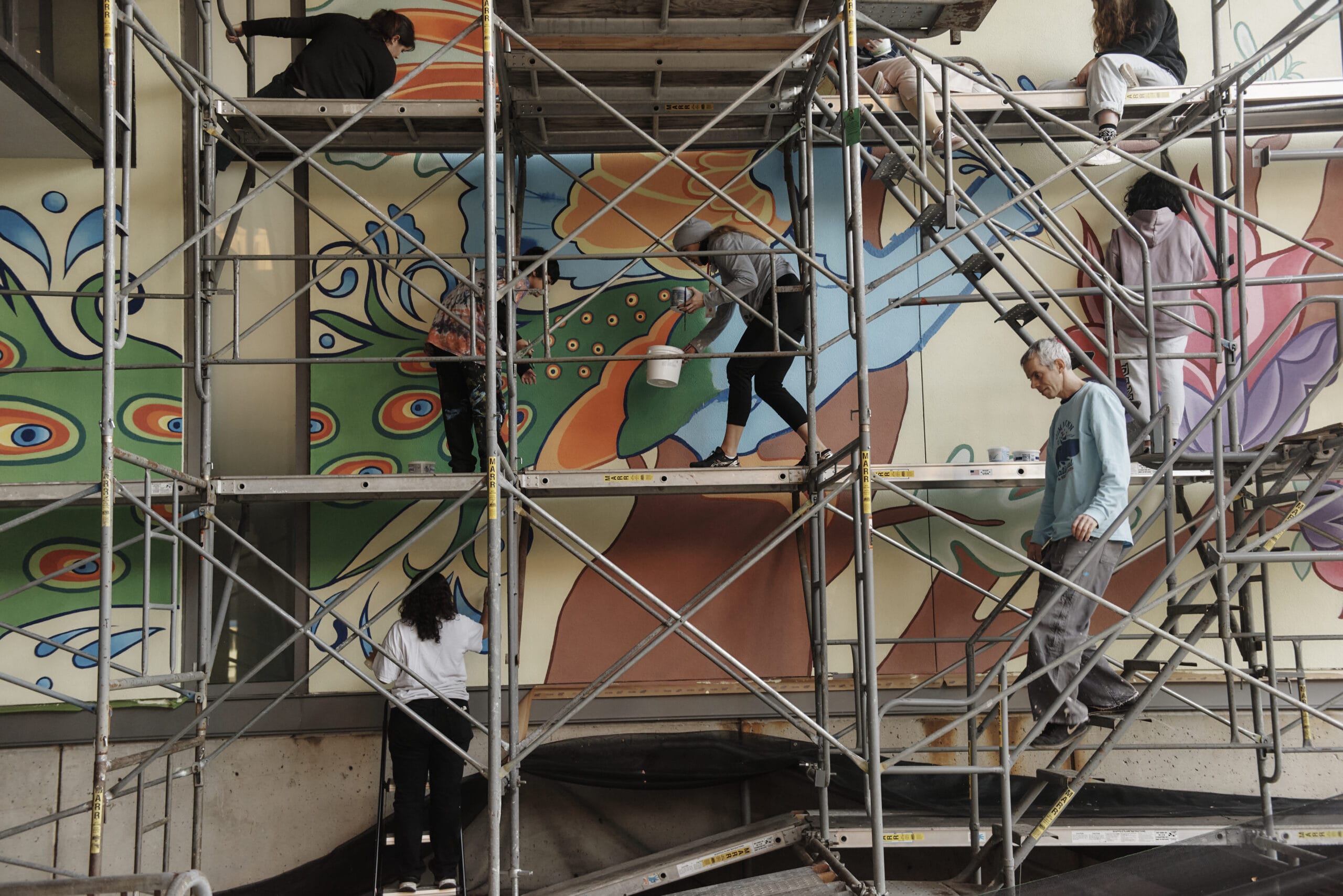 People stand on scaffolding painting a mural at MassArt.
