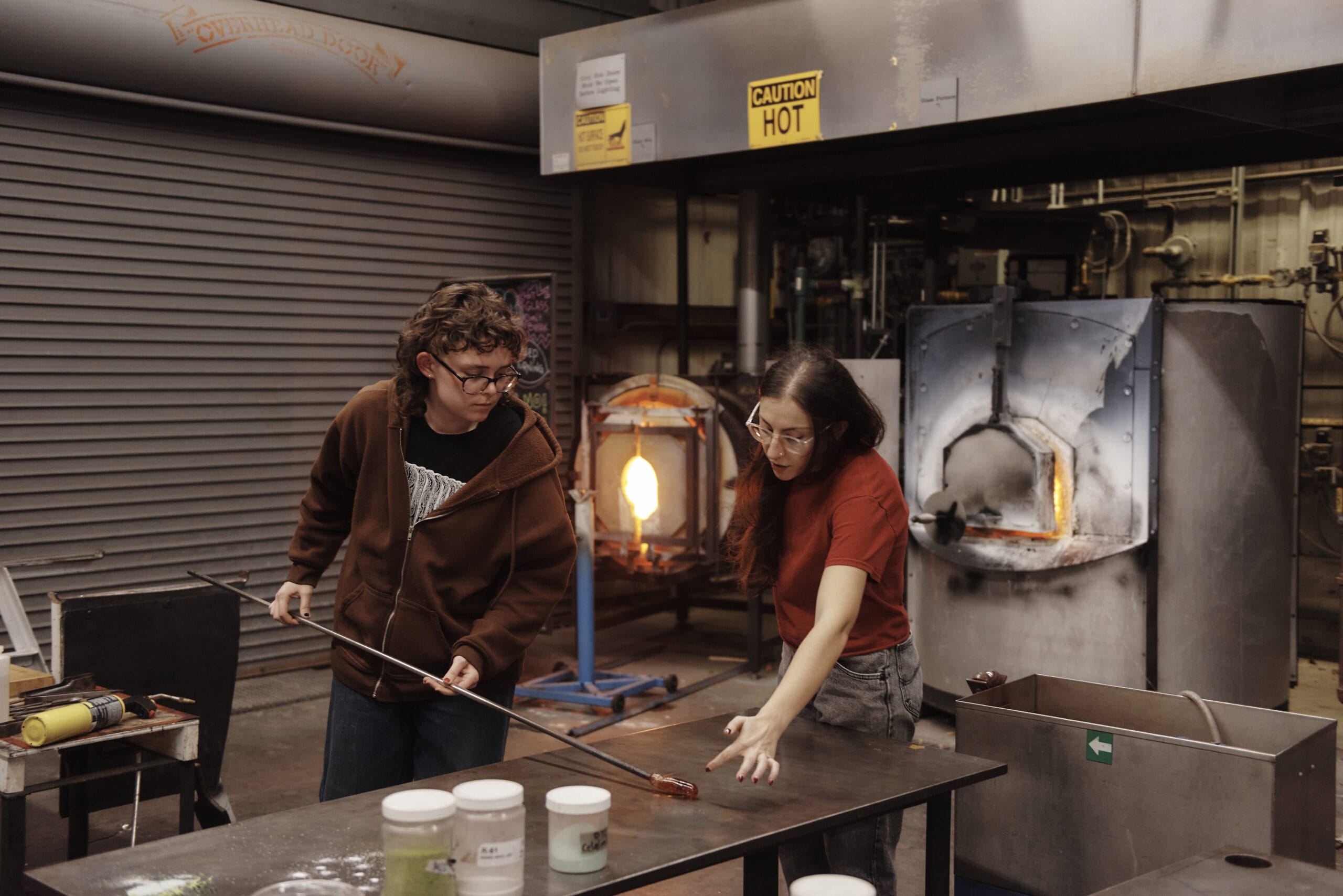 A faculty member instructs a student on how to blow glass.