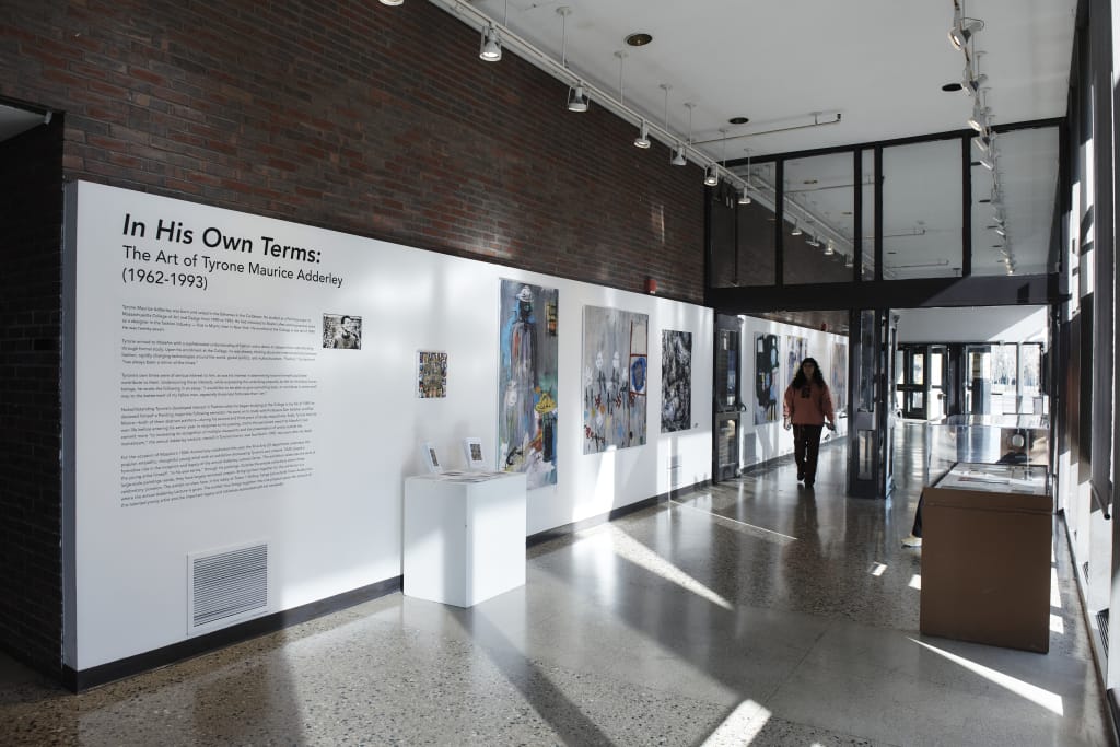 A long, brick hallway with white gallery walls and artwork hung along it.