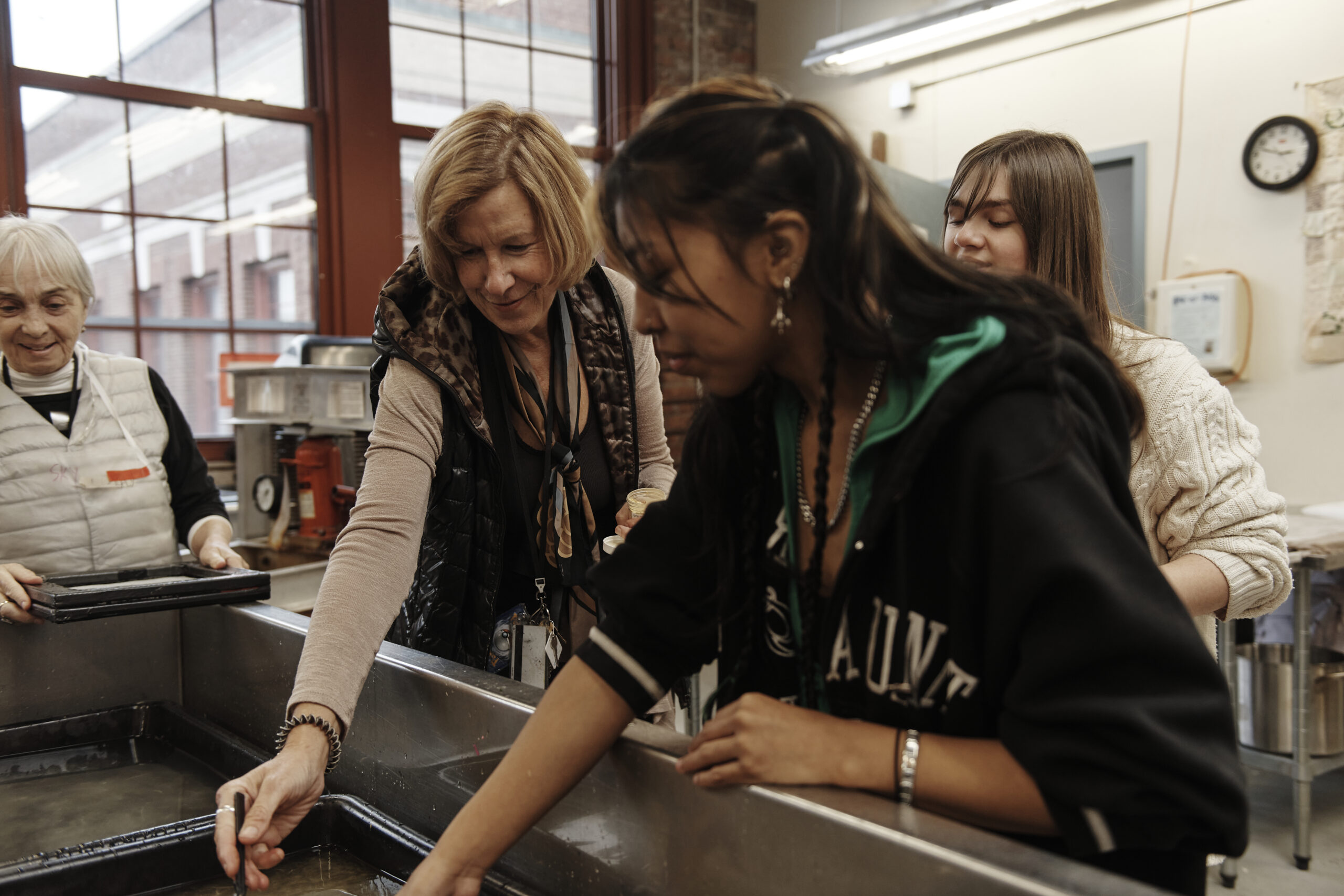 A faculty member leans in to help a student with the papermaking process.