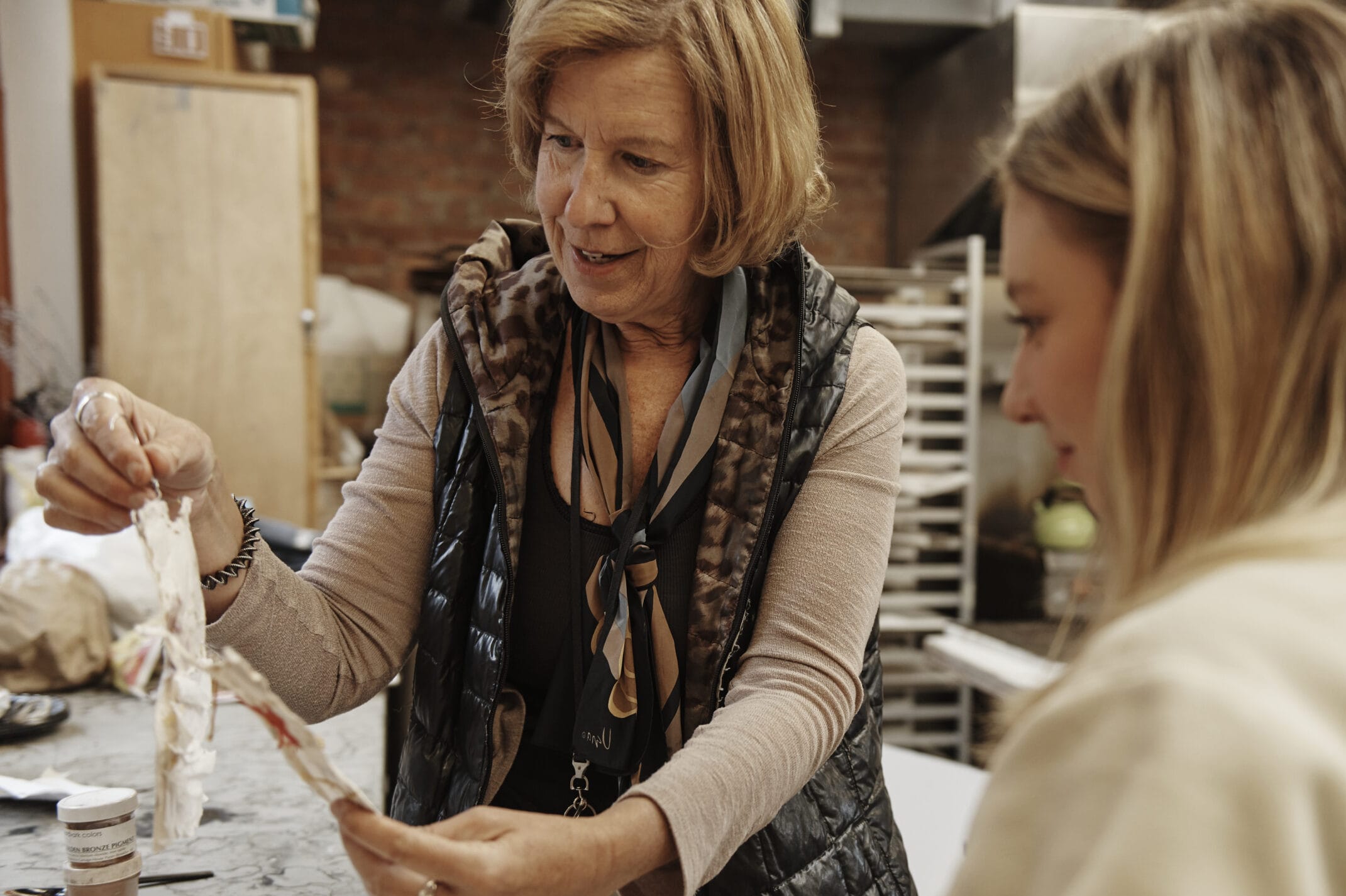 A faculty member holds up a piece of artwork while chatting with a student in her class.