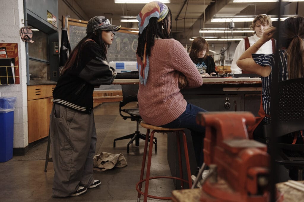 A student leans over a table surrounded by students in the Jewelry and Metalsmithing shop.