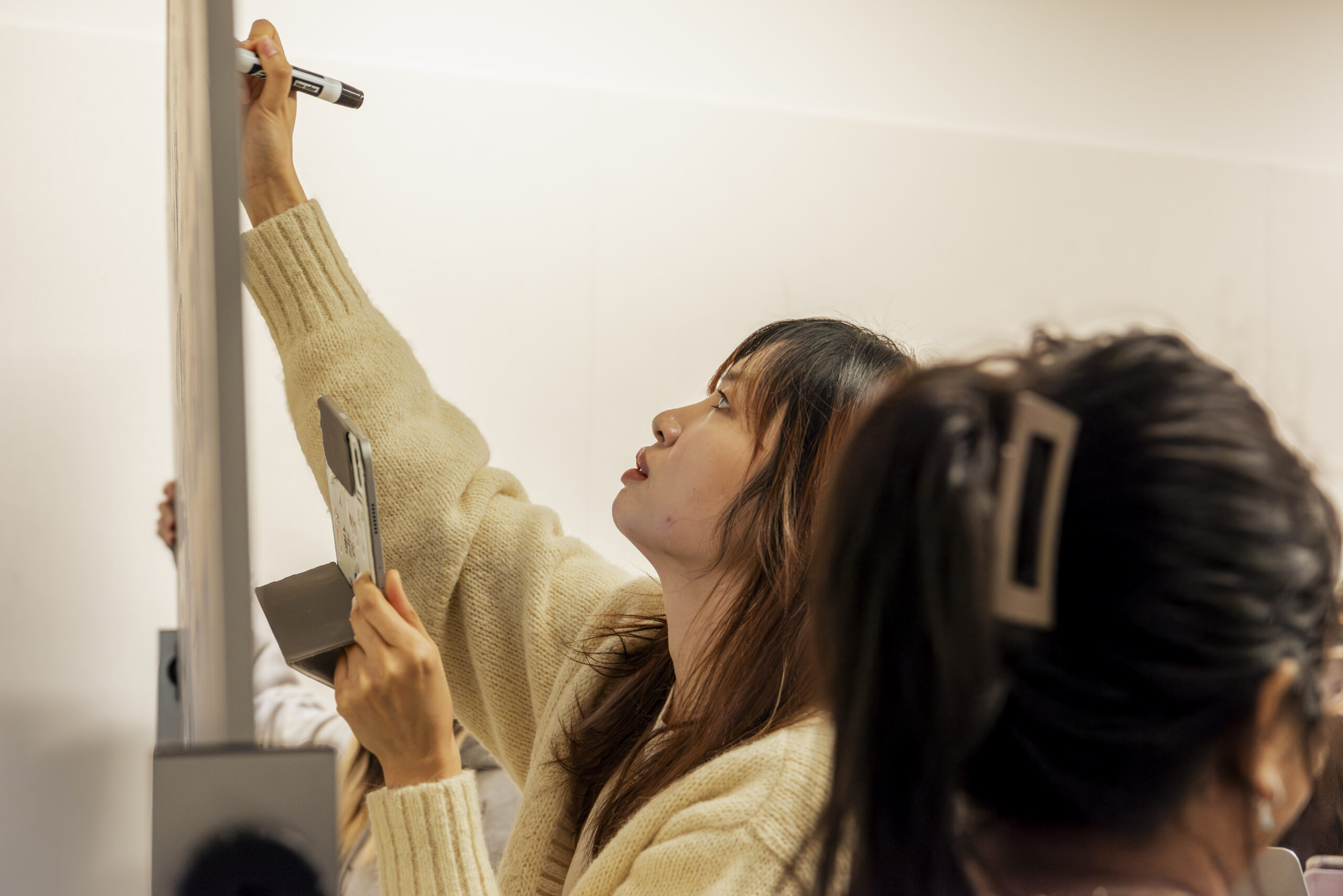 A student reaches up to write on a white board.
