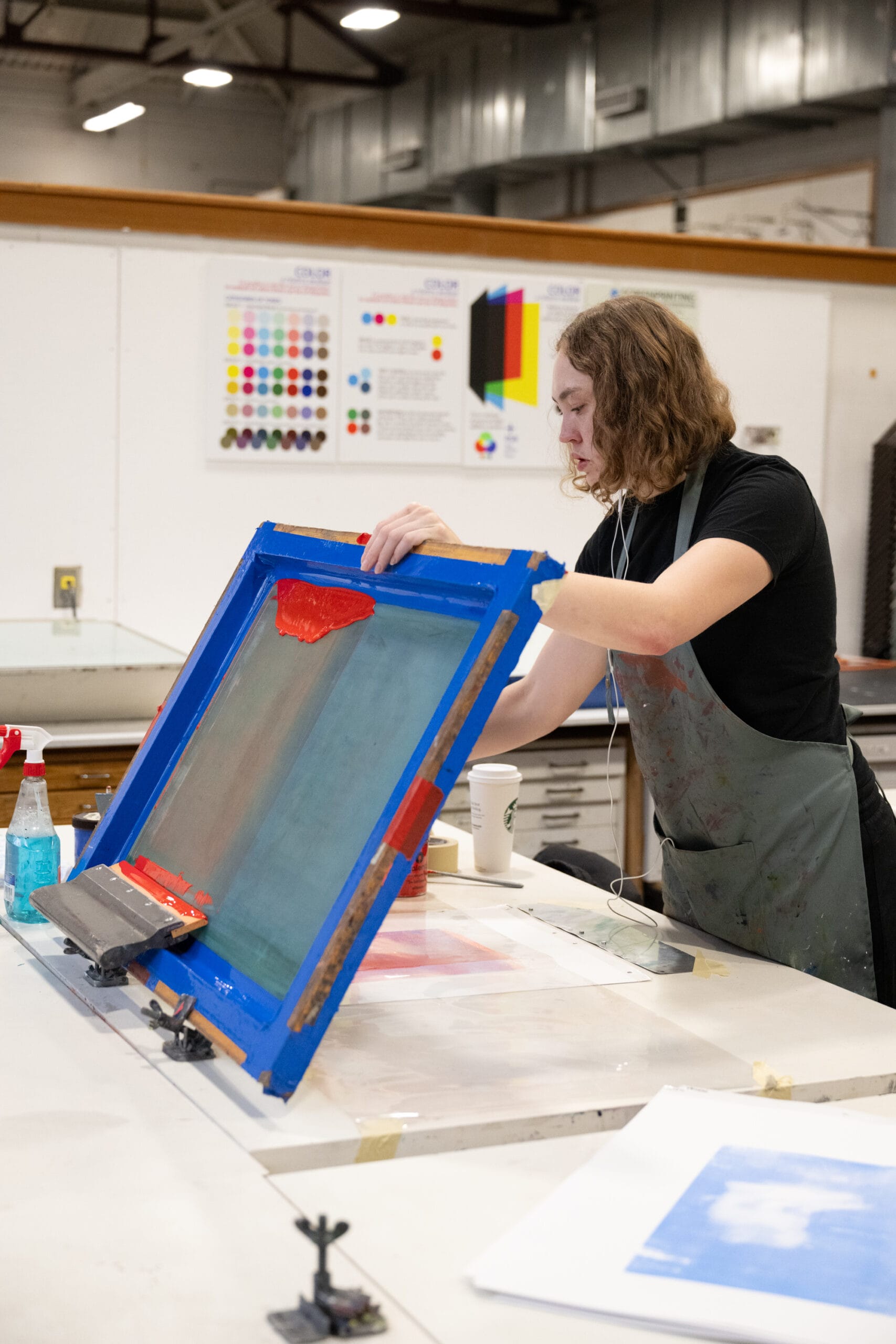 A student lifts her silkscreening frame to adjust her paper.