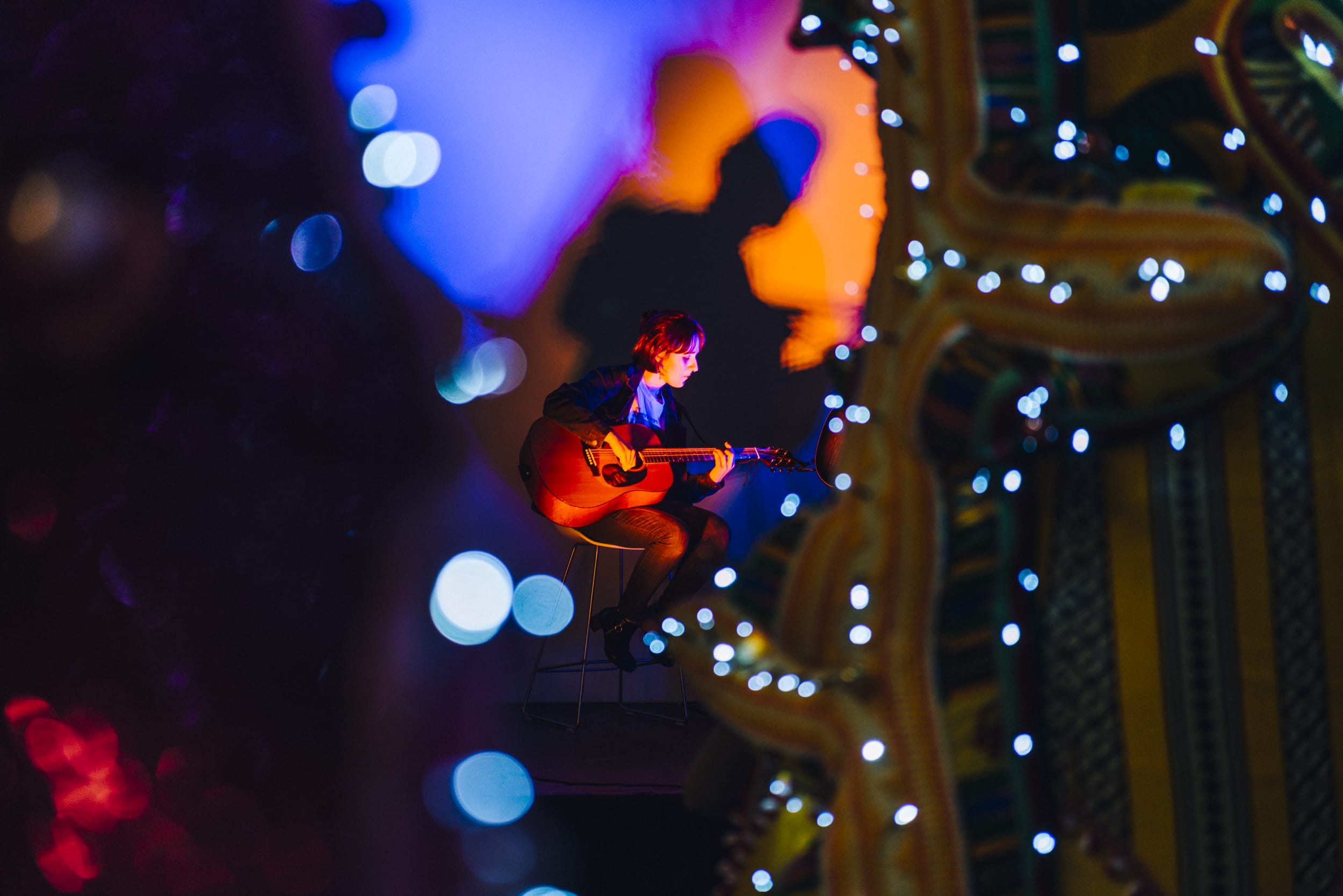An abstract photo of colorful lights being cast on a person playing guitar in a dark setting.