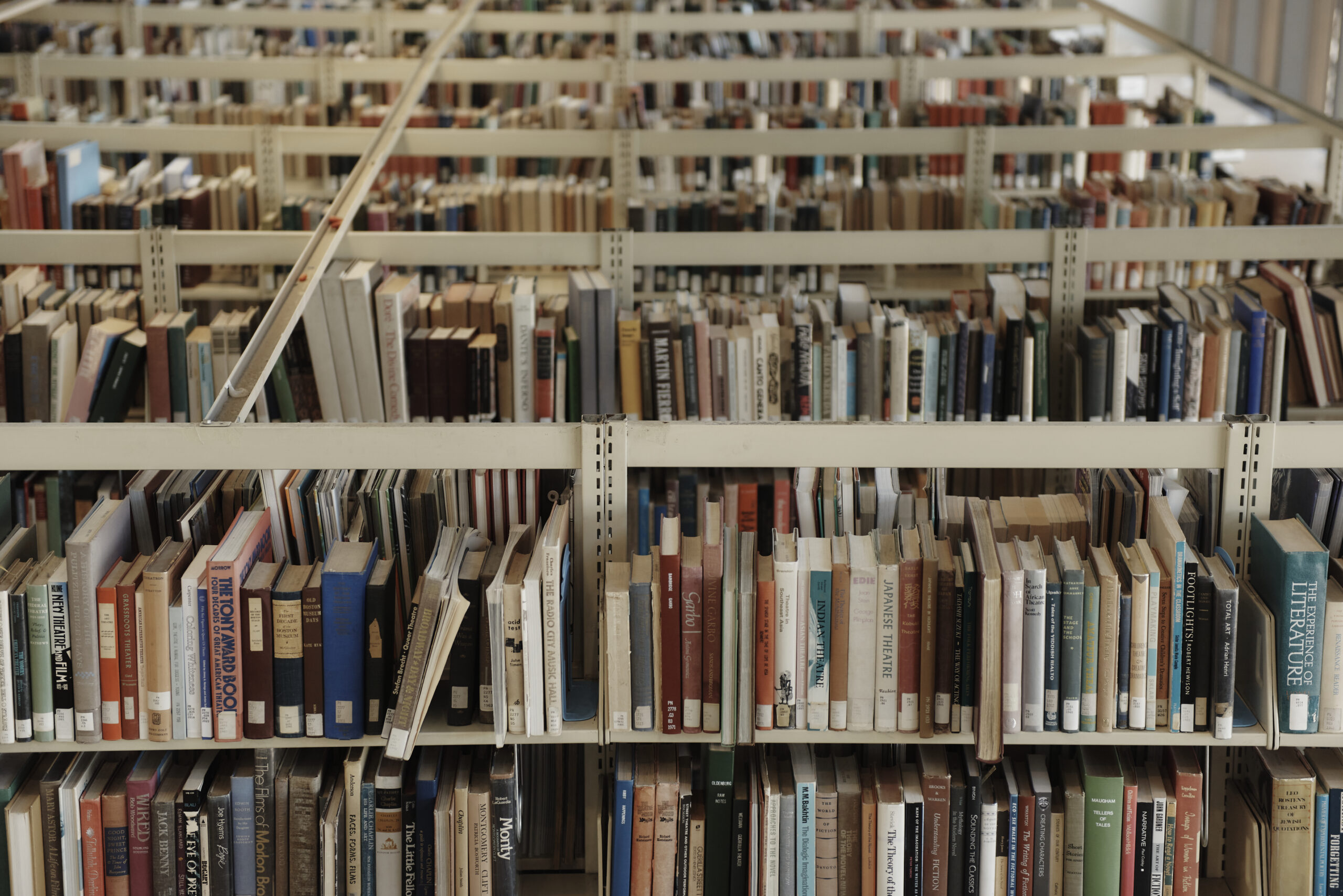 Rows of bookshelves filled with various books in a library, viewed from above. The shelves are densely packed with books of different colors and sizes, creating a pattern of spines and titles.