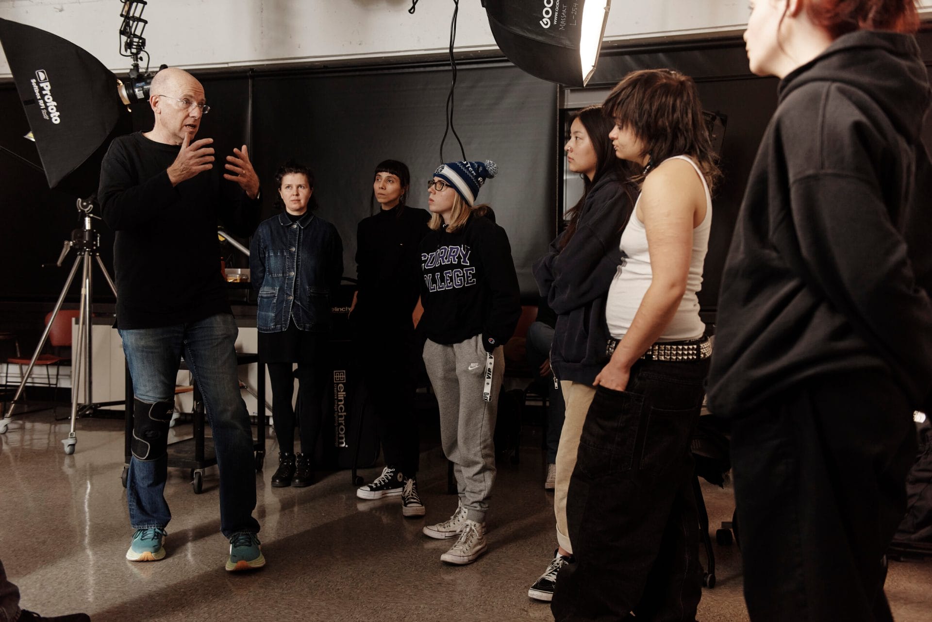 Students stand in a photography lighting studio listening to their instructor.