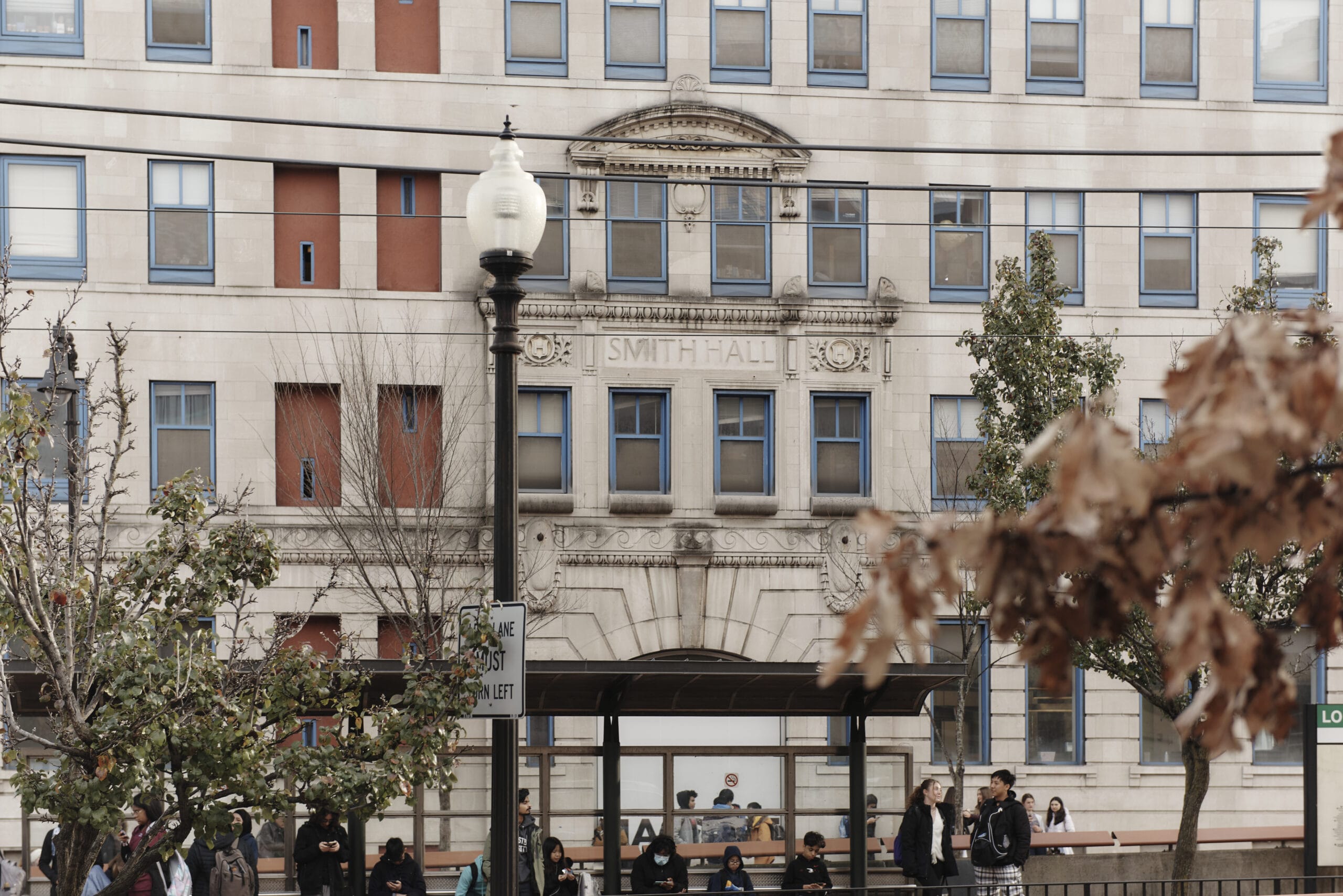 Photo of a street-level MBTA train stop with a large residence hall building behind it.