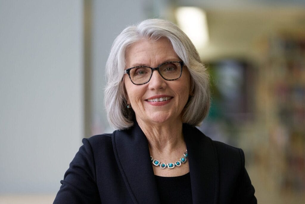 President Mary Grant stands in the library, with her arm on a high-top table.