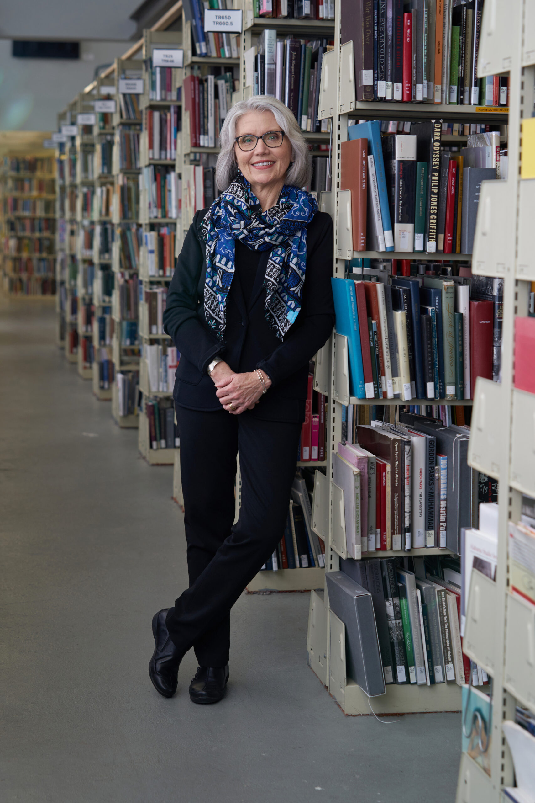 MassArt President Mary Grant leans against a bookshelf in the stacks at the Library.