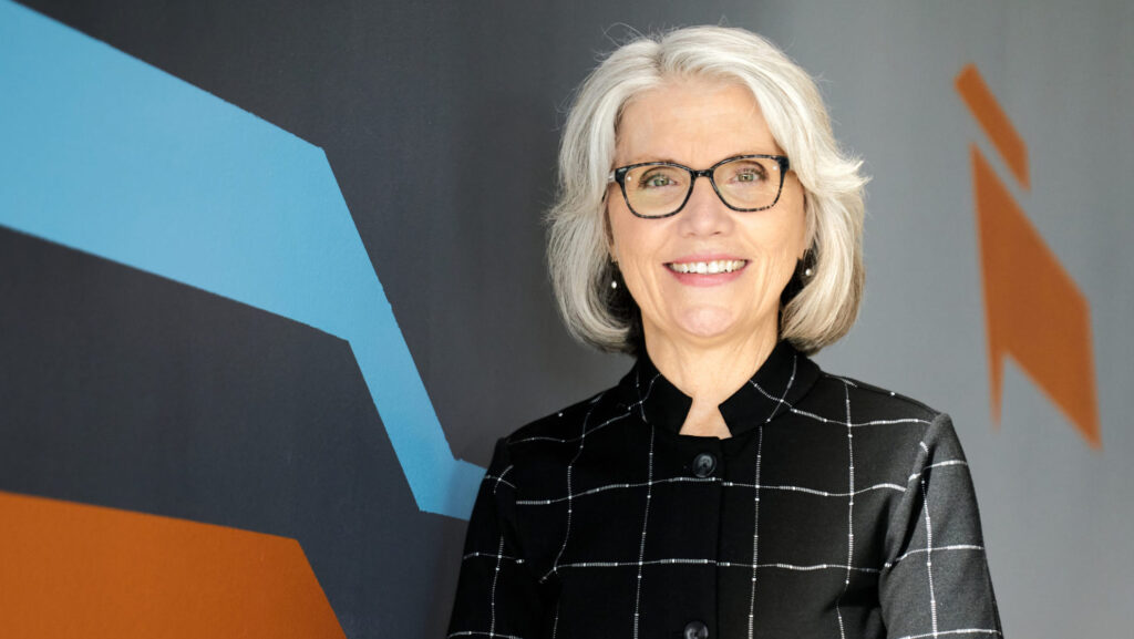 President Mary Grant standing in the front of the "Intrepid" mural in MassArt's Design and Media Center.