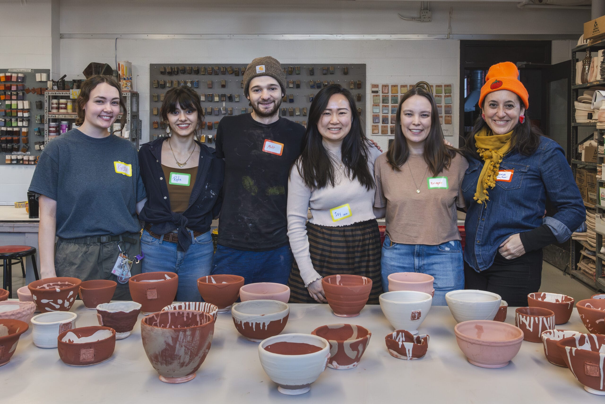 Students and staff line up smiling behind a table of freshly glazed ceramic bowls.