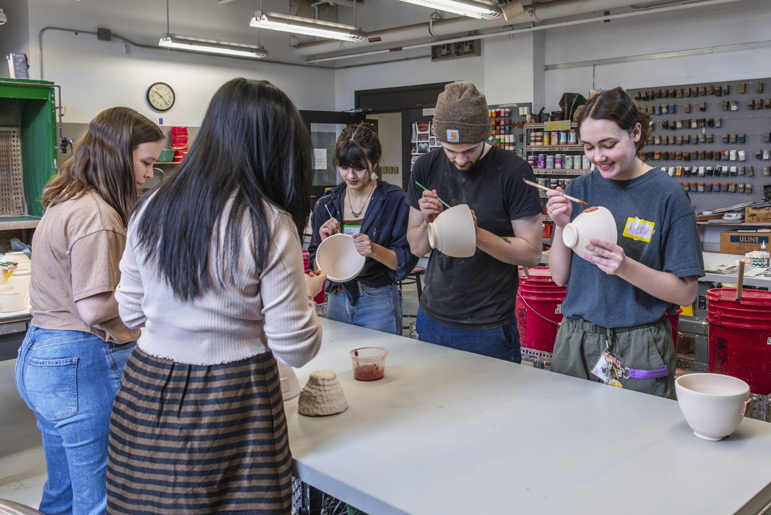 People standing around painting pottery bowls with glaze.