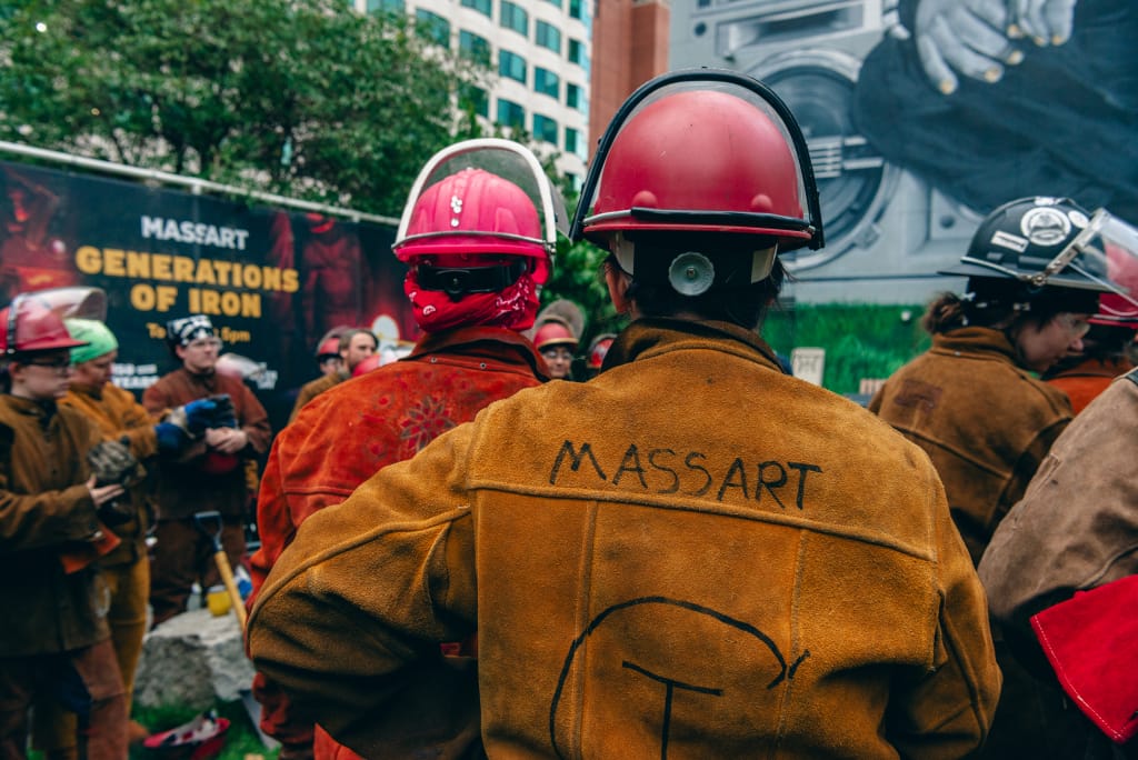 The backs of people in the iron corps, one with a leather jacket with "MassArt" written on the back.