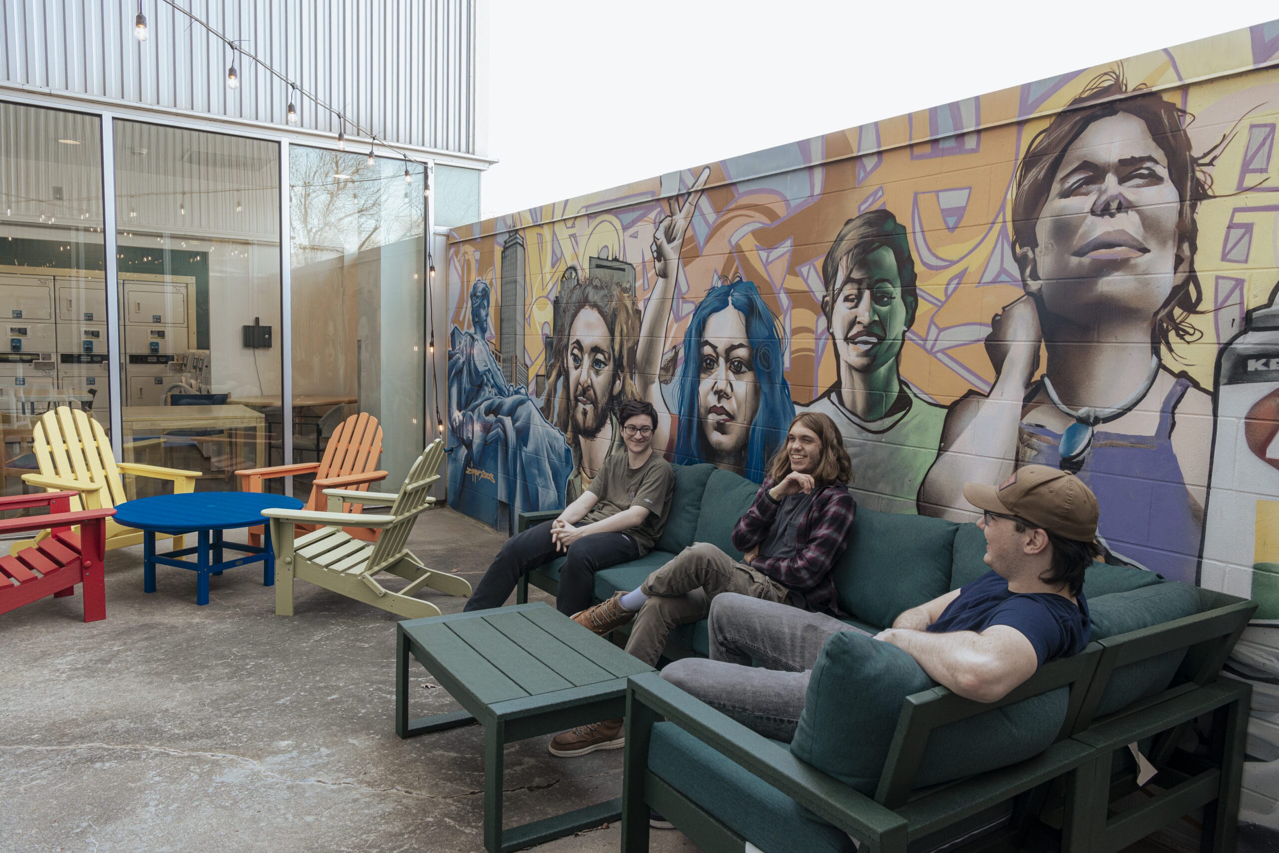 Students lounge in an outdoor courtyard on lounge furniture, with a mural of faces behind them.