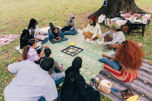 People sit on a blanket outside talking and playing games.