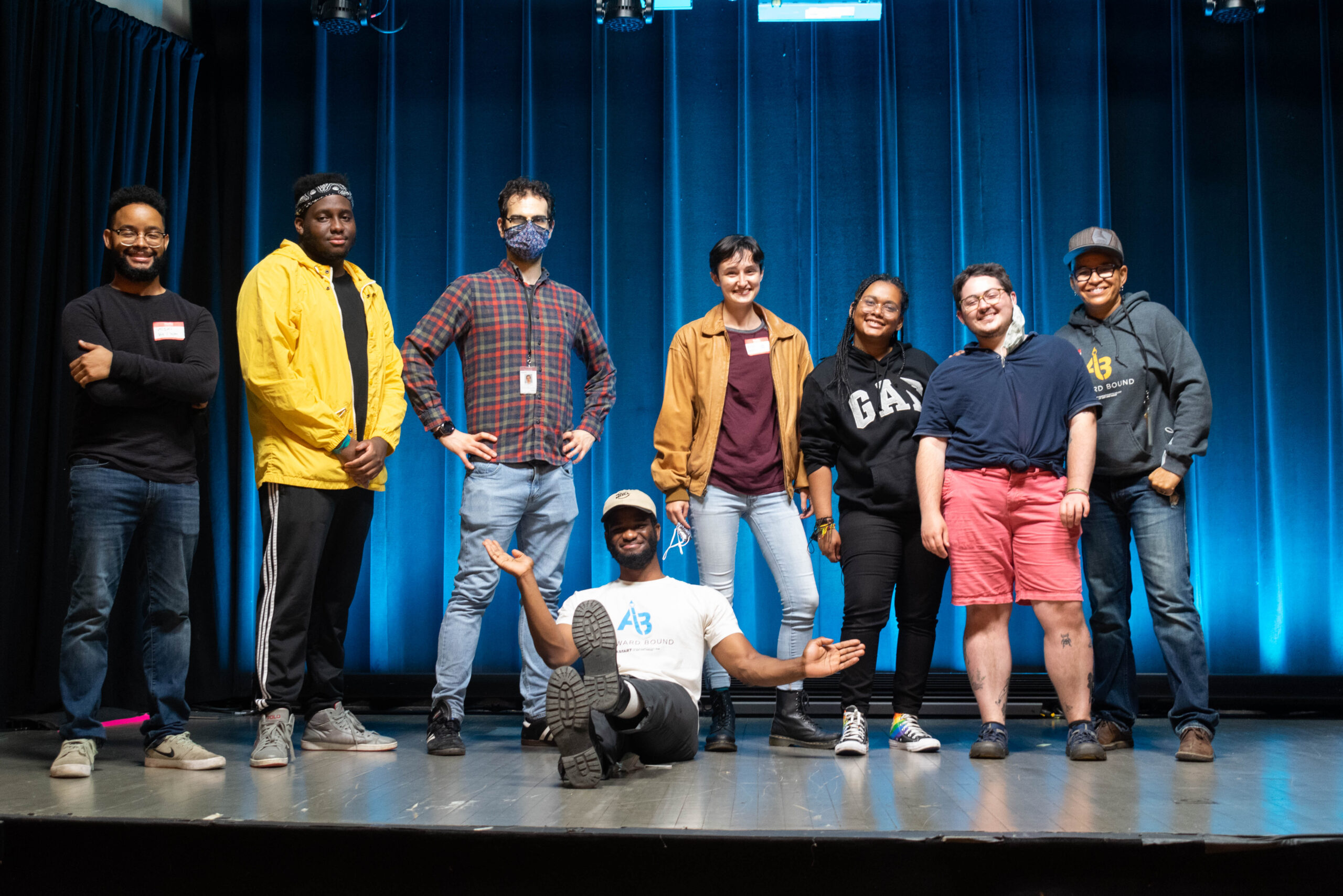 Artward Bound Students and Staff are lined up on a stage smiling with a blue curtain behind them.