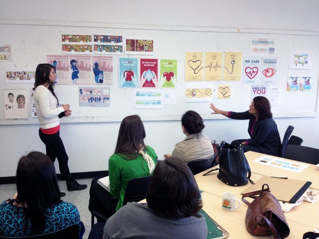 A students stands next to a wall of designs centered around public health in a classroom.
