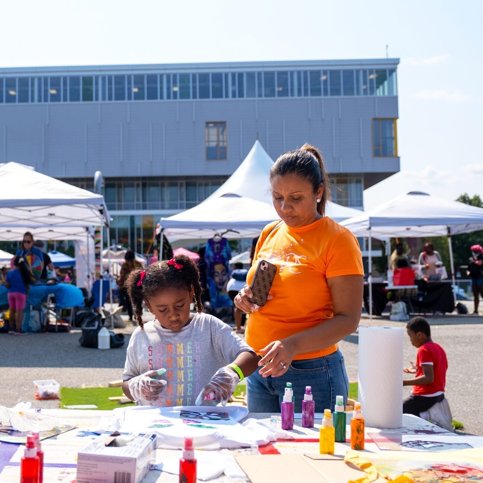 A woman stands with a little girl at an arts table.