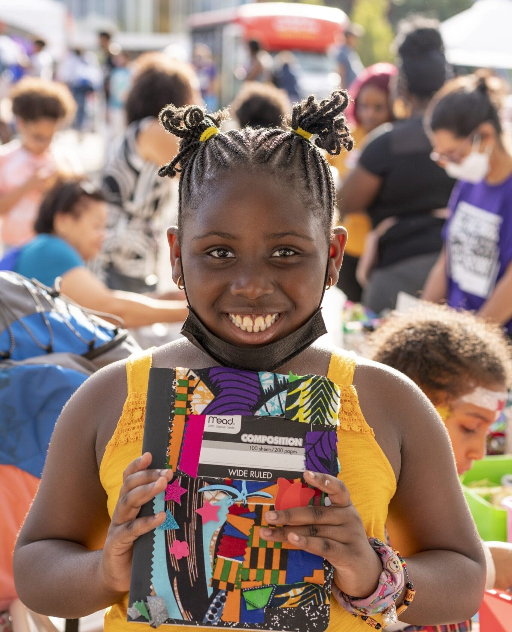 A little girl smiling while holding a colorful notebook.