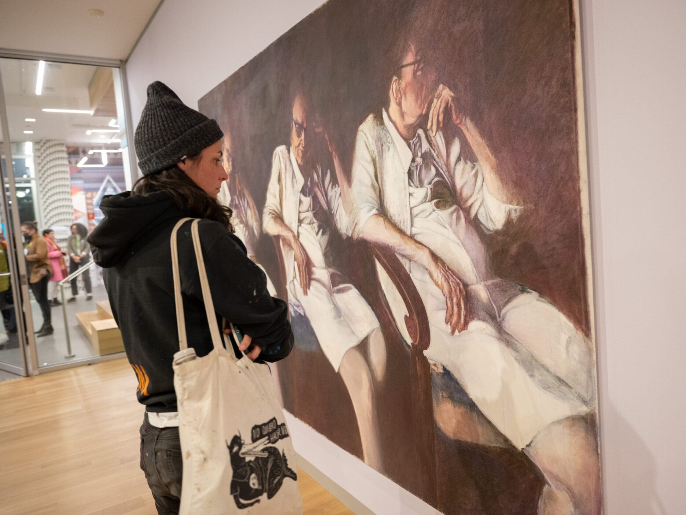 A woman in a beanie studies a painting up close.