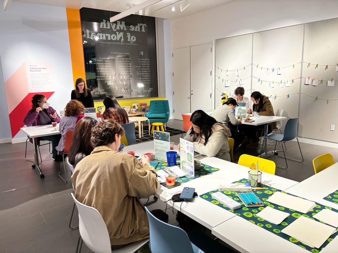 A room of tables with people sitting down and concentrating on making things.