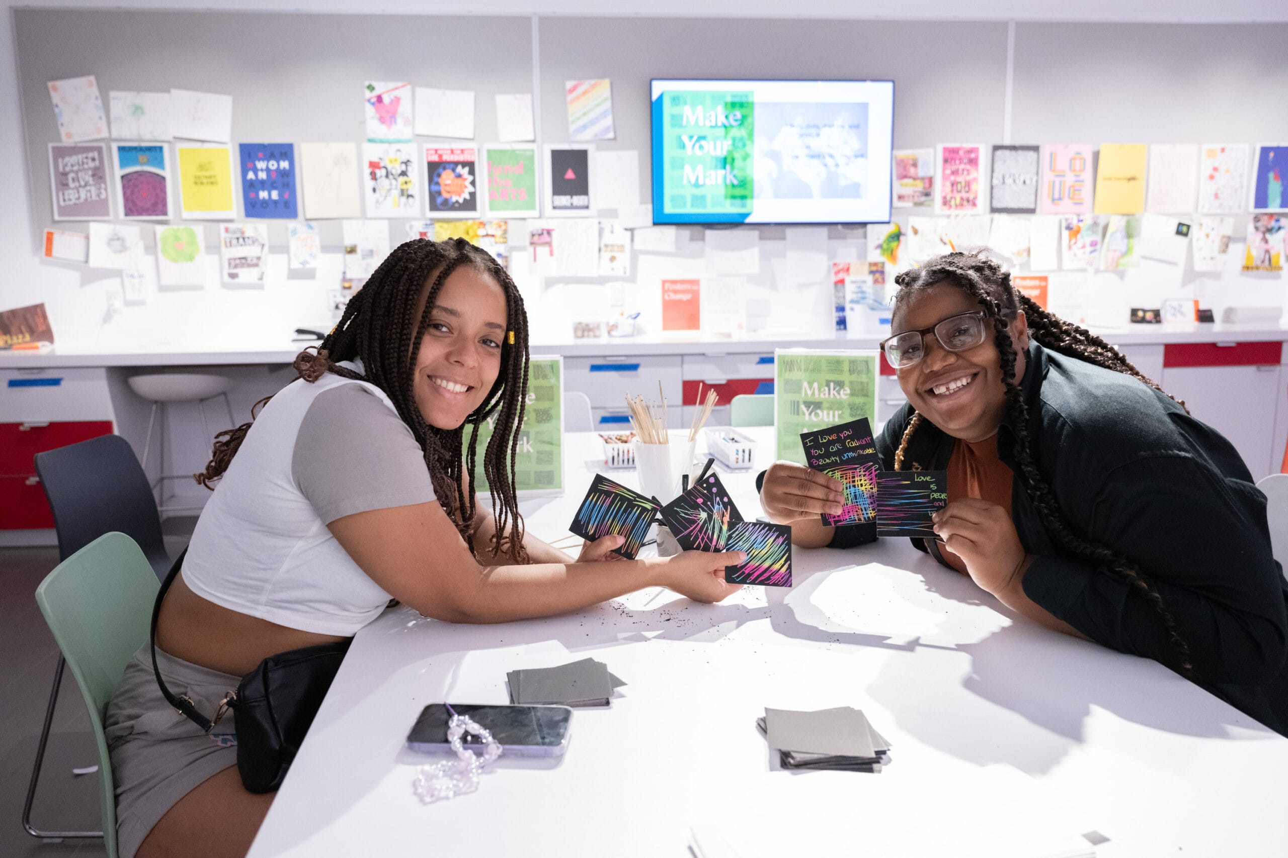 Two people sit creating art at a white table at an event at MassArt Art Museum.