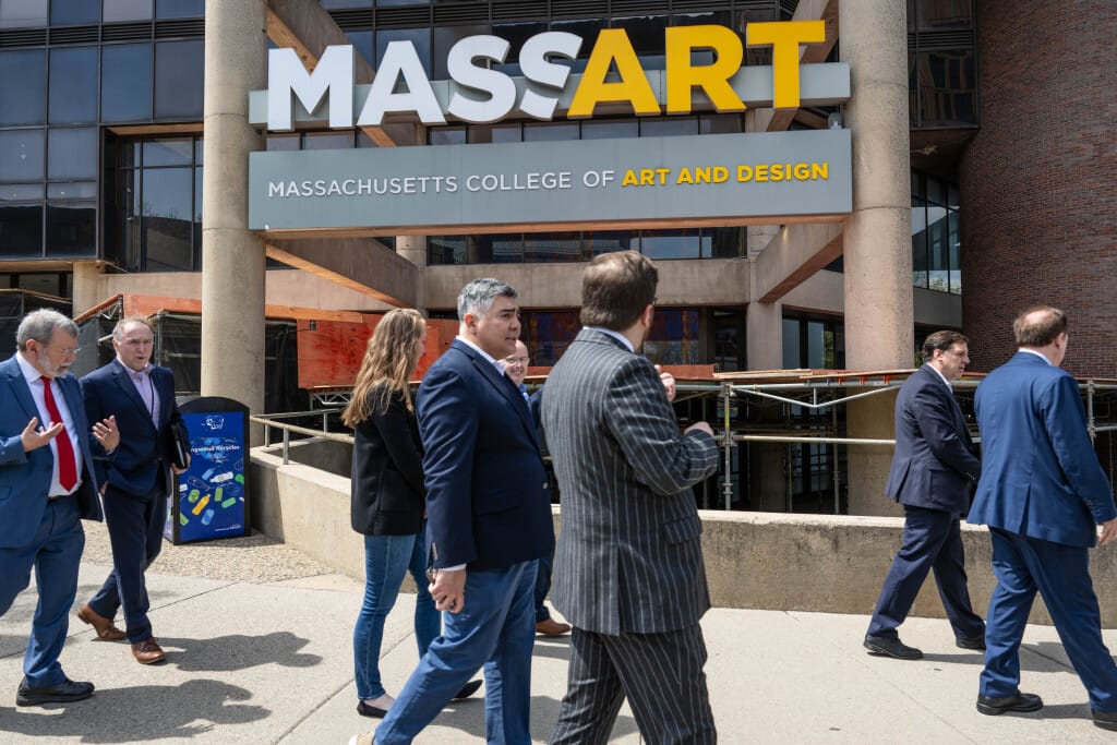 Professionals in business attire see walking down the sidewalk in front of the MassArt sign on the Tower building.
