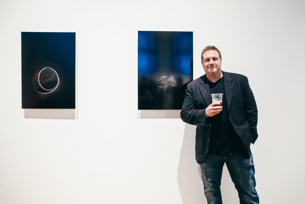 MassArt faculty member Marc Holland stands in front of two photographs hung on the wall.