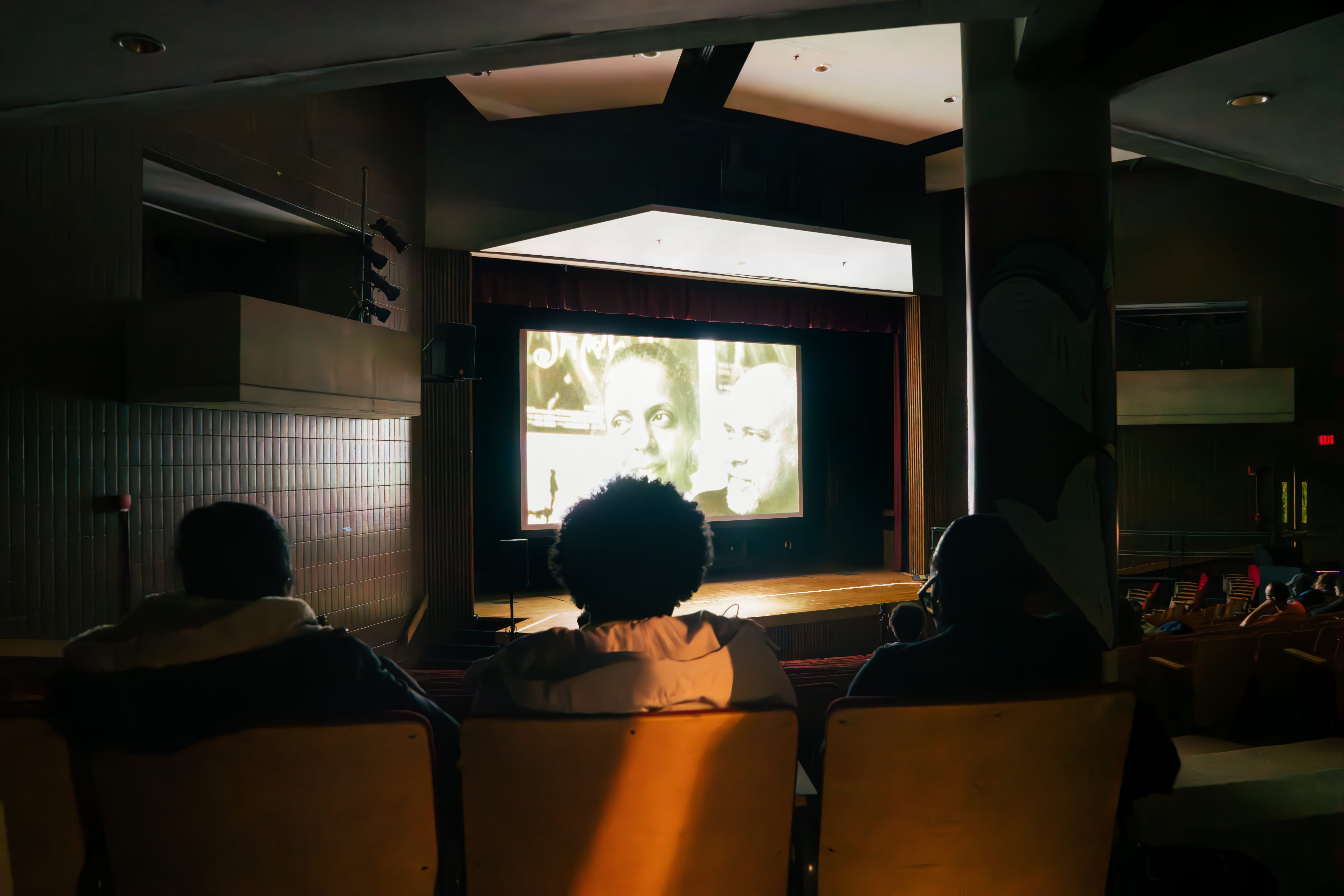 Silhouettes of a students sitting in an auditorium watching a movie on a large screen.