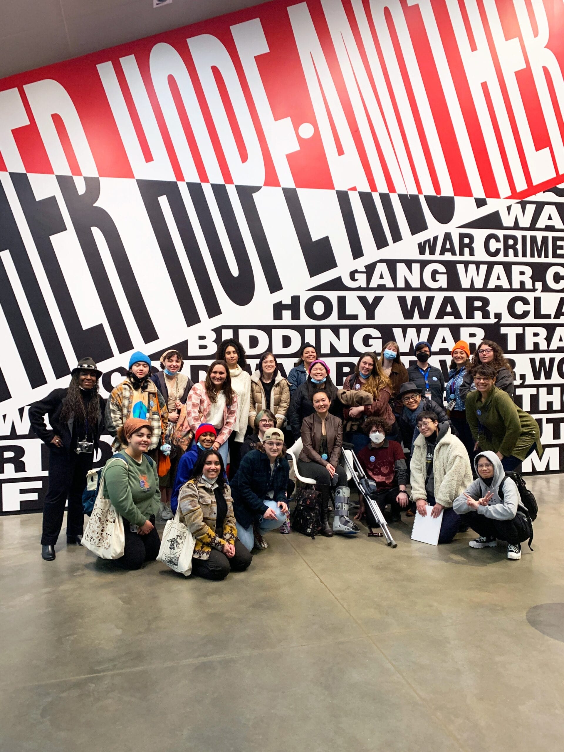 A group of students pose in front of a large black, white and red mural.
