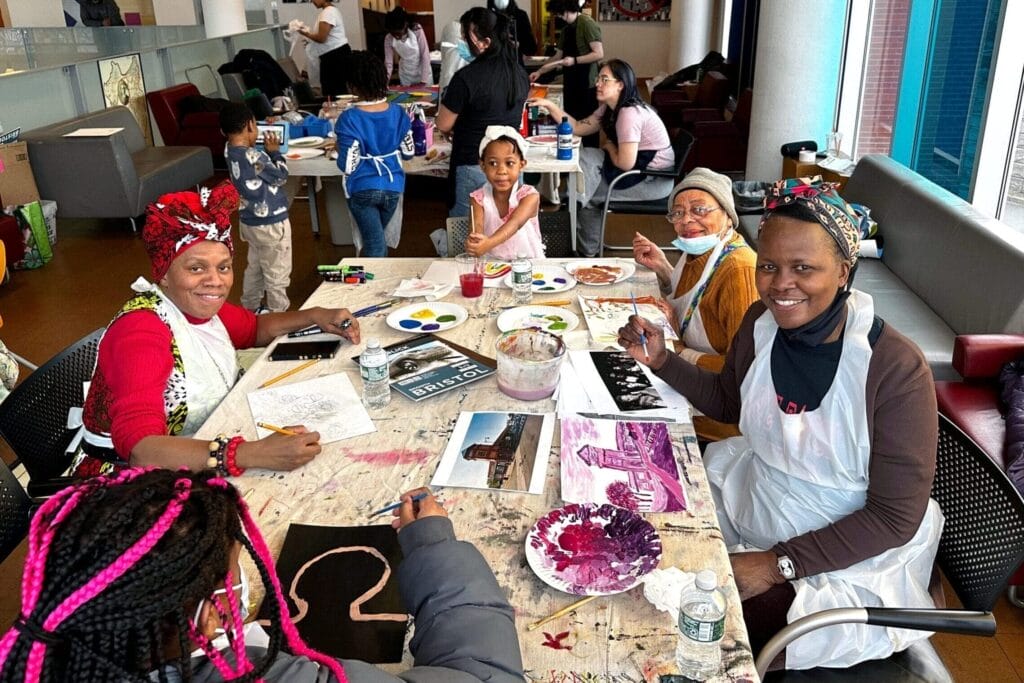 children and adults sit around a table painting and smiling