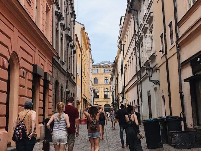 A group of people, perhaps on one of those immersive travel courses, strolls down a narrow cobblestone street lined with colorful historic buildings. The sky is clear, and the architecture features arched windows and ornate details.