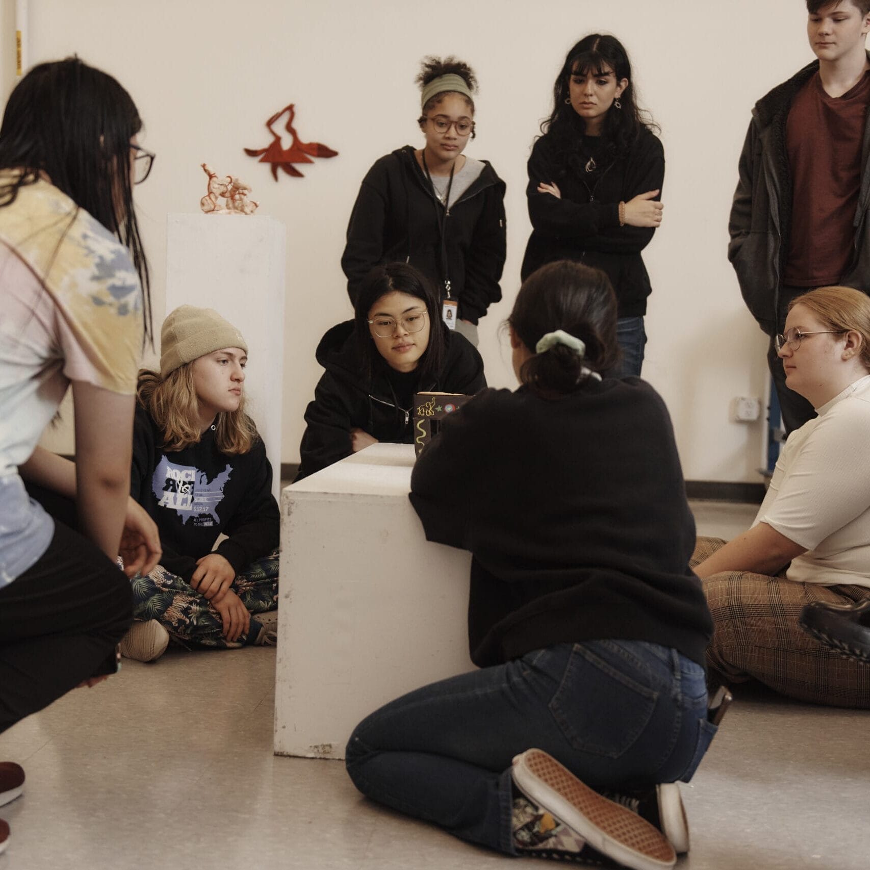Students lean in to look at a piece of artwork on a pedestal in a gallery space.