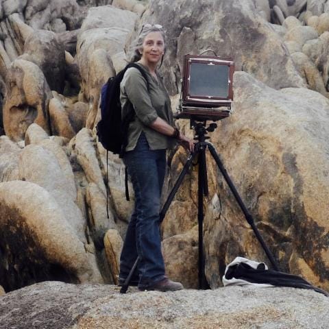 Photo of Laura McPhee standing with a large format camera on some boulders