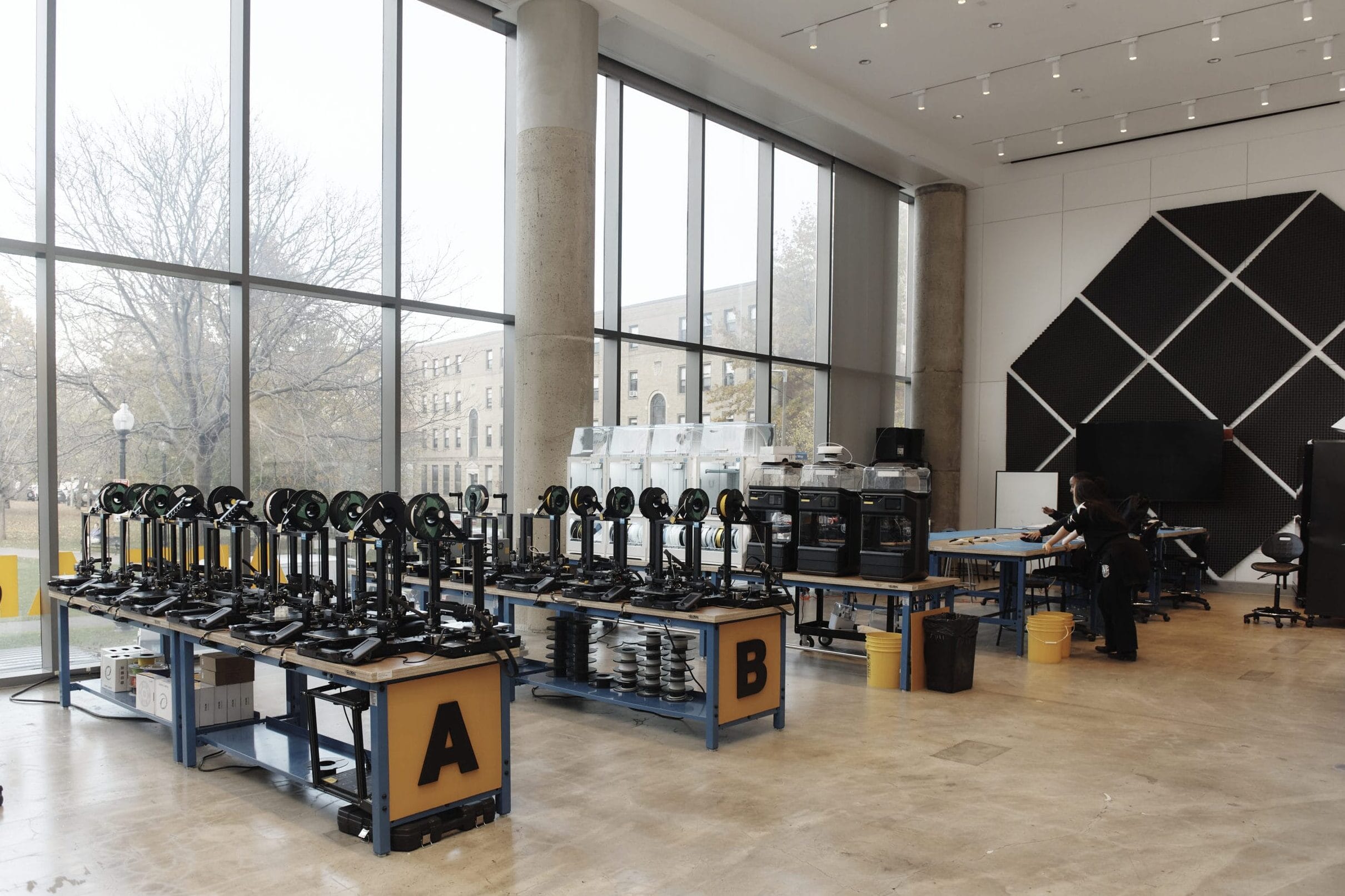 An expansive room with high ceilings and large windows houses one of MassArt's FABLABS, equipped with 3D printers and wirebenders.