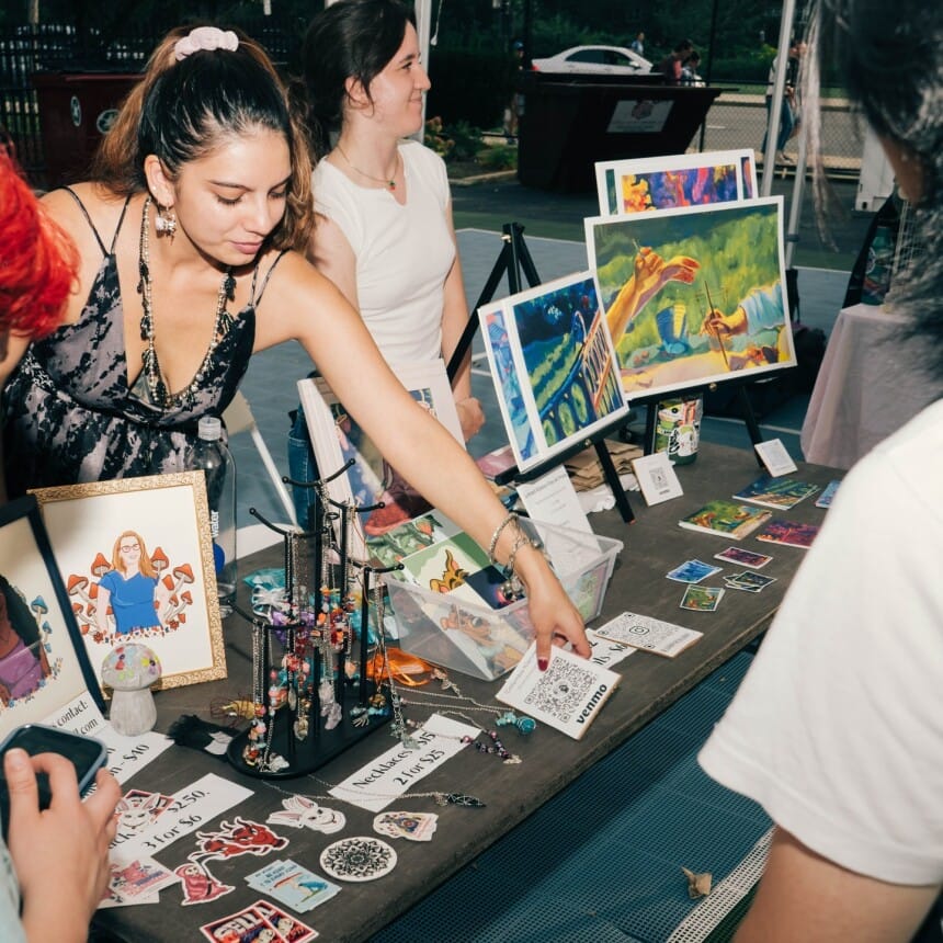 An artist adjusting her table of work for sale at the MassArt Night Market.