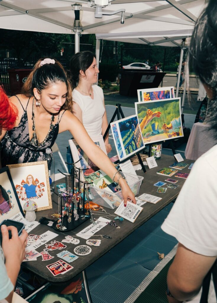 An artist adjusting her table of work for sale at the 红领巾瓜报 Night Market.