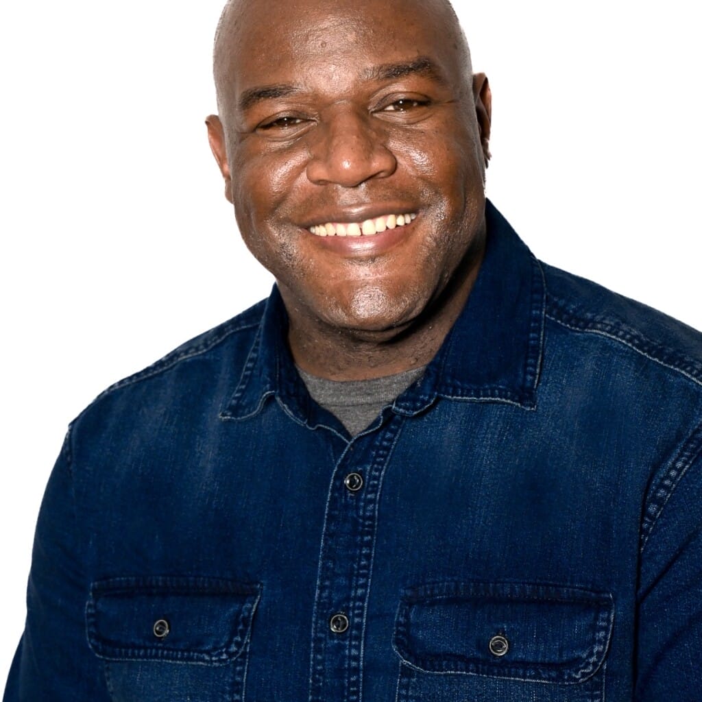 Smiling man in a dark denim shirt against a white background.