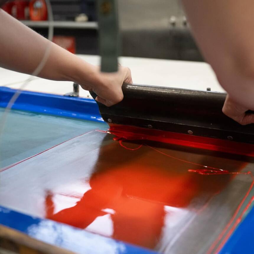 Hands shown pushing ink across a silkscreen.