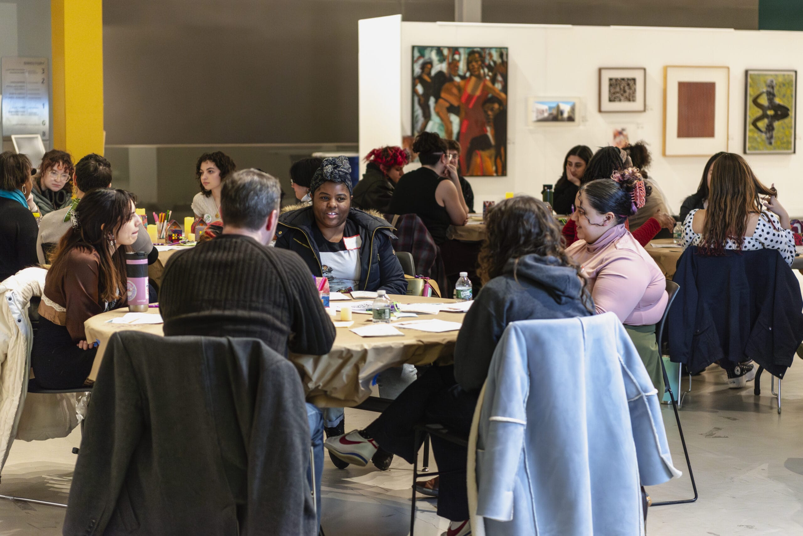 People sitting at round tables with artwork hanging on the walls in the background.