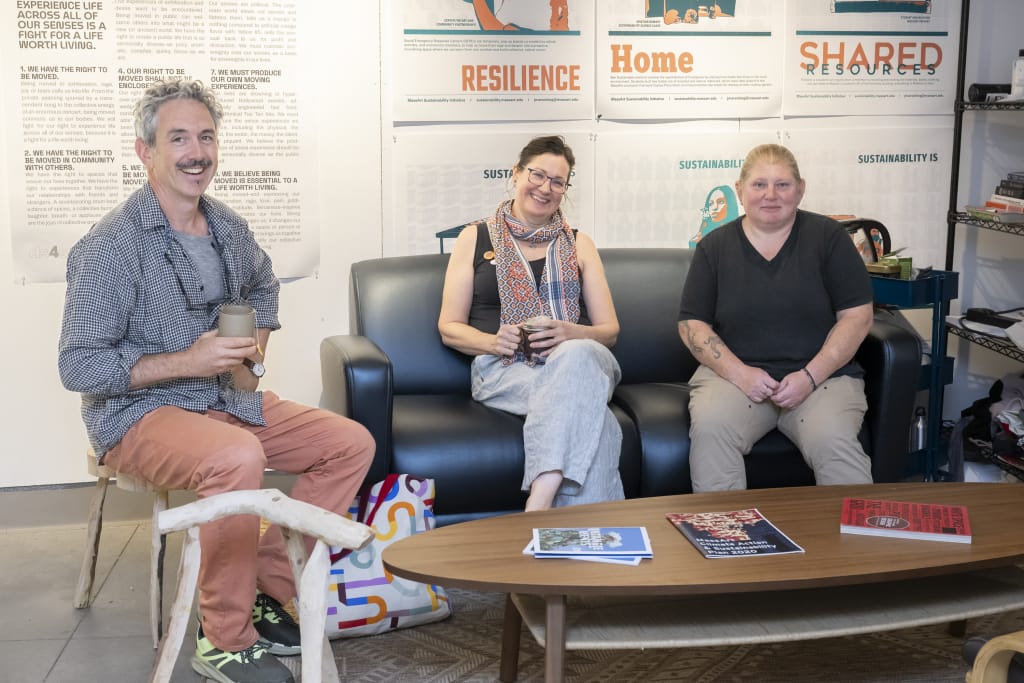 3 faculty members smiling at the camera, while sitting together on a couch in a lounge area.