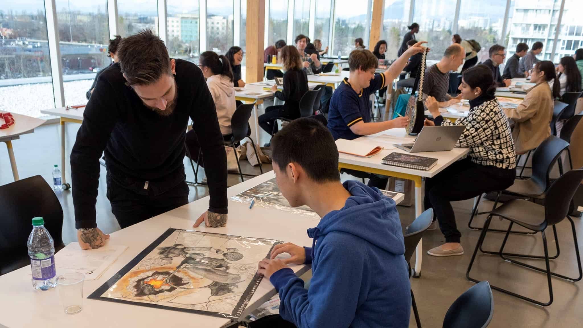 In a bustling Boston classroom, students immerse themselves in art projects at tables, while a teacher offers guidance. The windows frame a dynamic cityscape, echoing the collaborative energy reminiscent of National Portfolio Day.