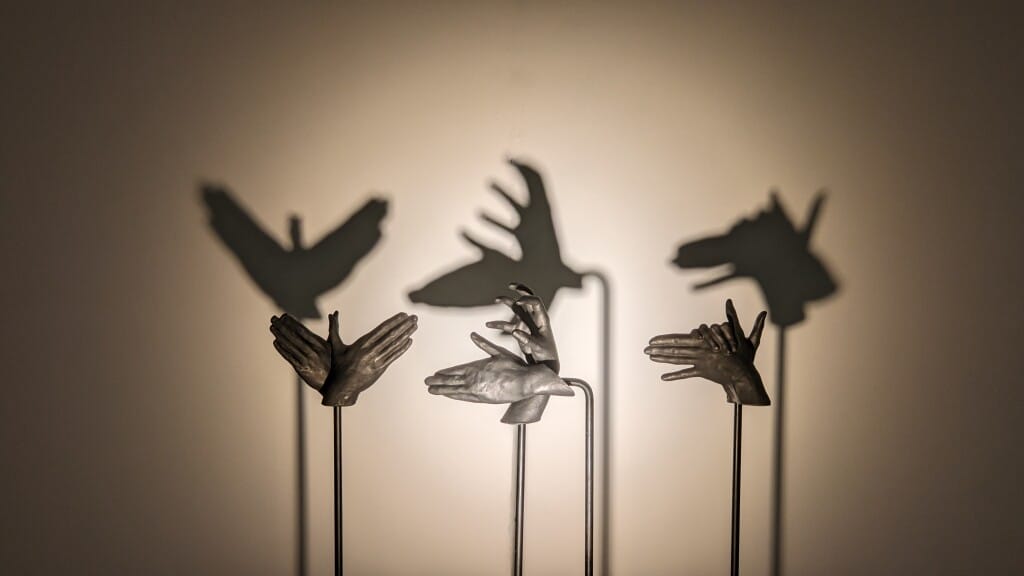 Hands cast out of iron sculpted in shapes that make shadow puppets appear on the wall behind them.