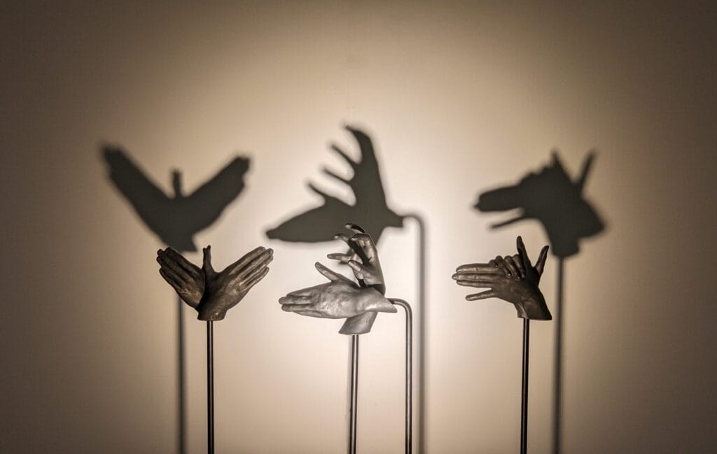 Hands cast out of iron sculpted in shapes that make shadow puppets appear on the wall behind them.