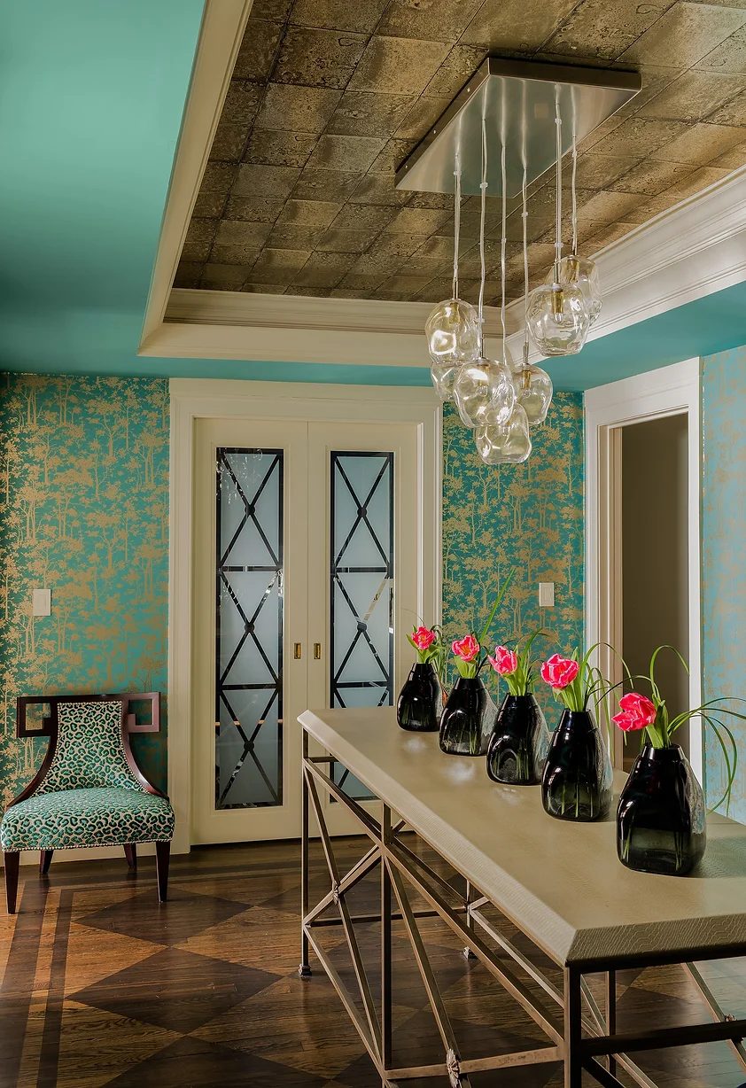 A photo of an aqua room with cream details and a long table with pink flowers in black vases.