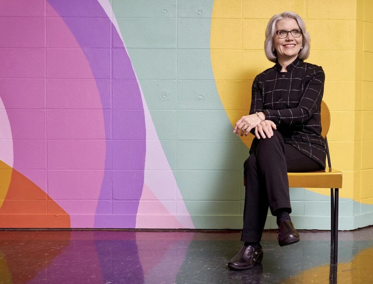 President Mary Grant sitting on a bench in front of a colorful wall.