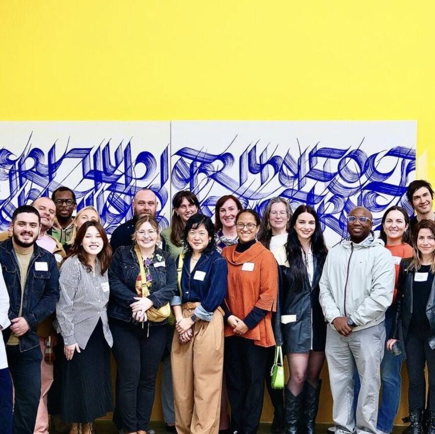 Alumni meetup group photo in a gallery setting in front of a yellow wall a large artwork.