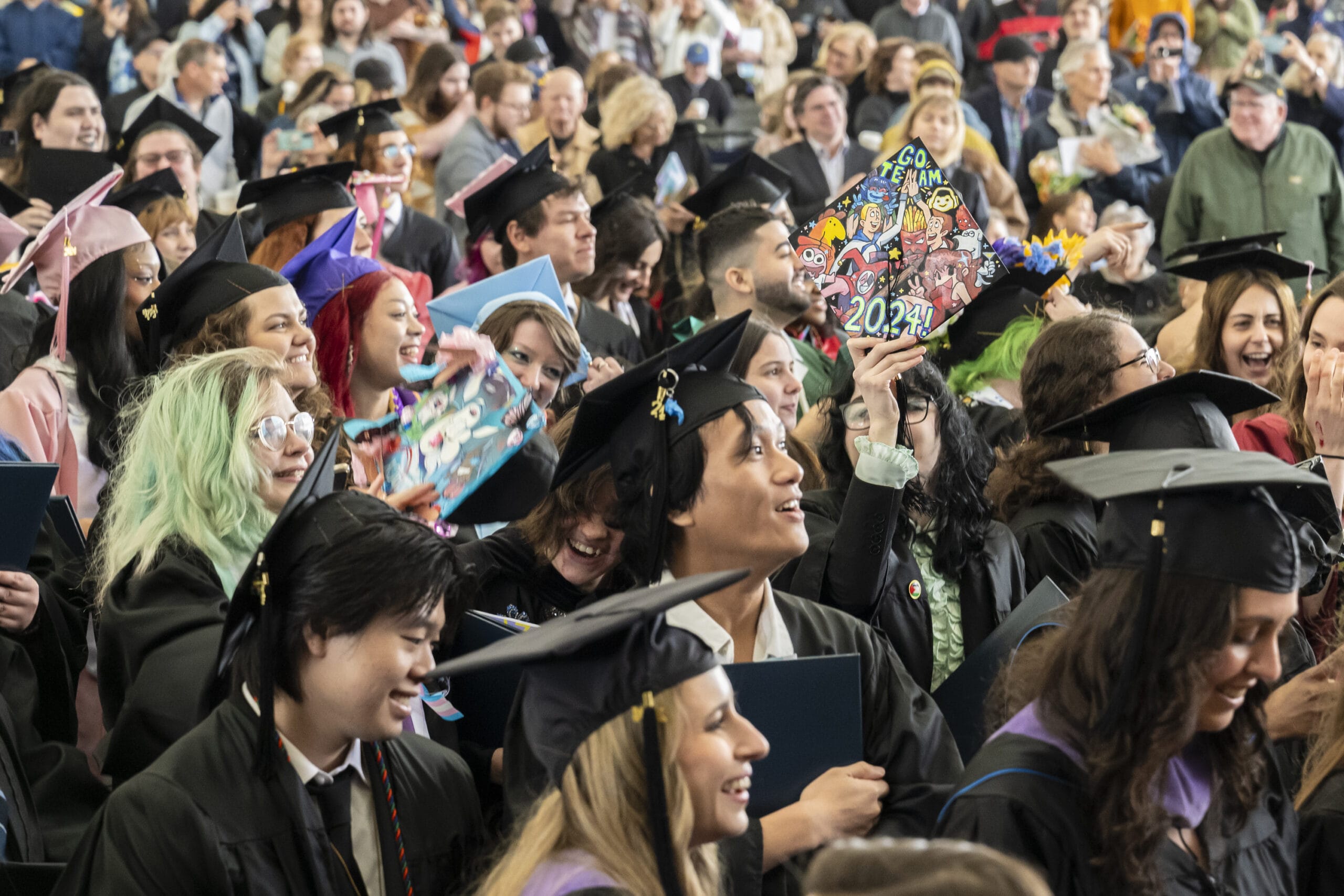 A crowd of graduates smile looking towards the stage