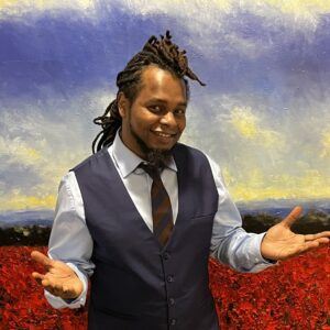 Man standing in a vest and tie shrugging in front of a painting.